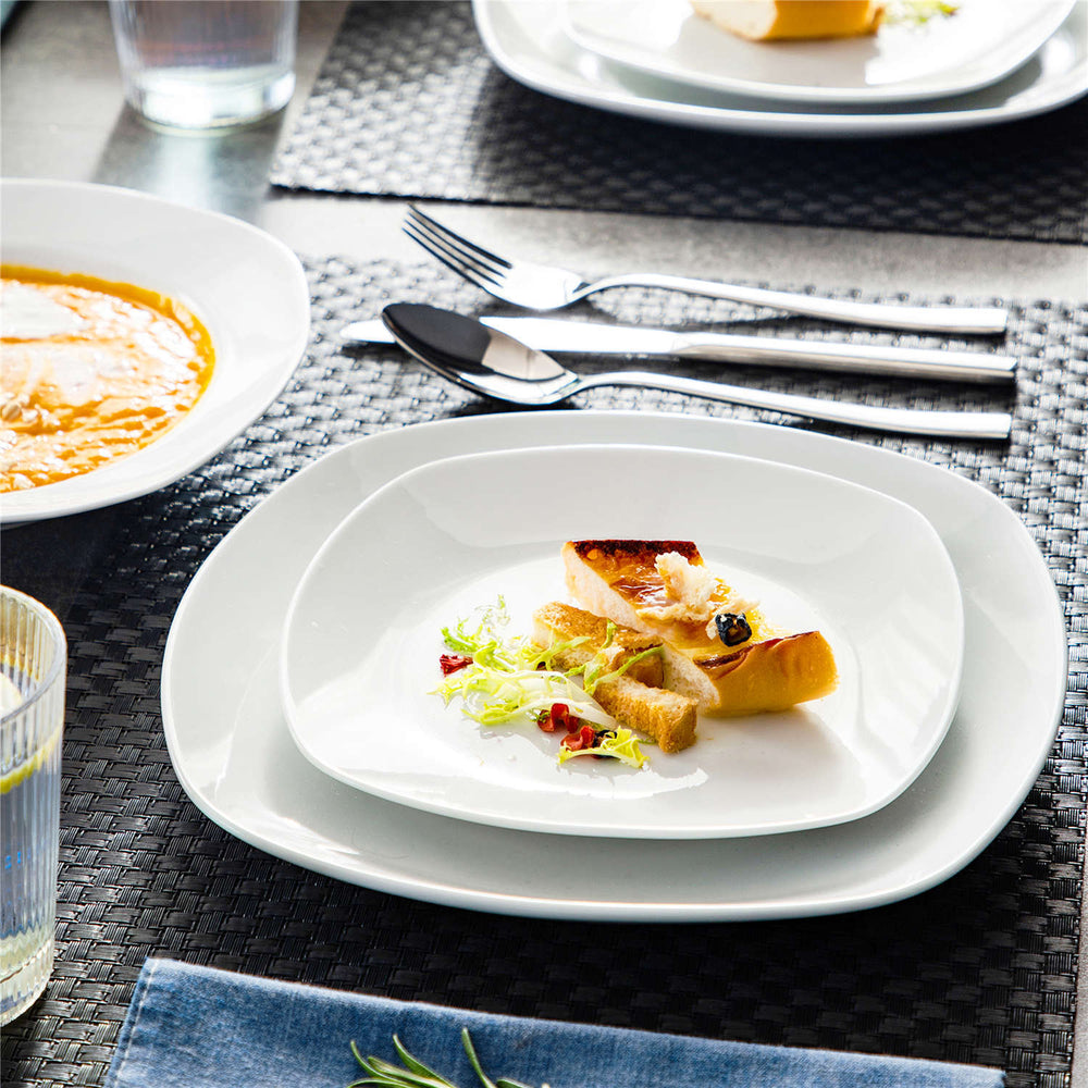 A set dining table with white plates and cutlery. One plate holds a gourmet meal of fish, bread, and salad