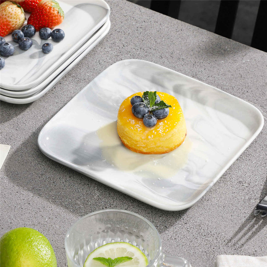 A small yellow dessert topped with blueberries and mint on a white square plate